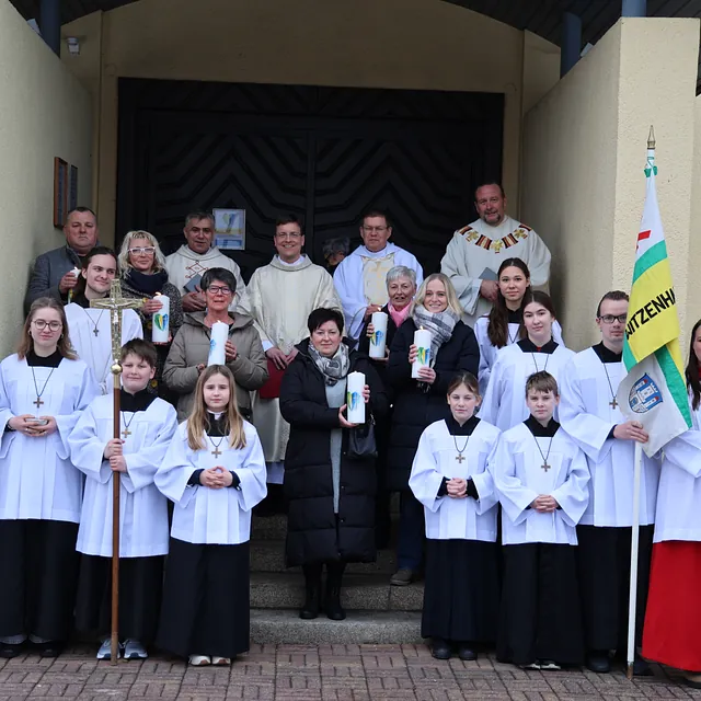 Gruppenbild der Prister, Messdiener und Ehrenamtlichen mit Kerzen vor der Kirche