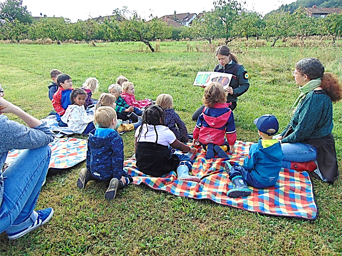 Kinder und Erzieherinnen Picknicken und lesen gemeinsam ein Buch